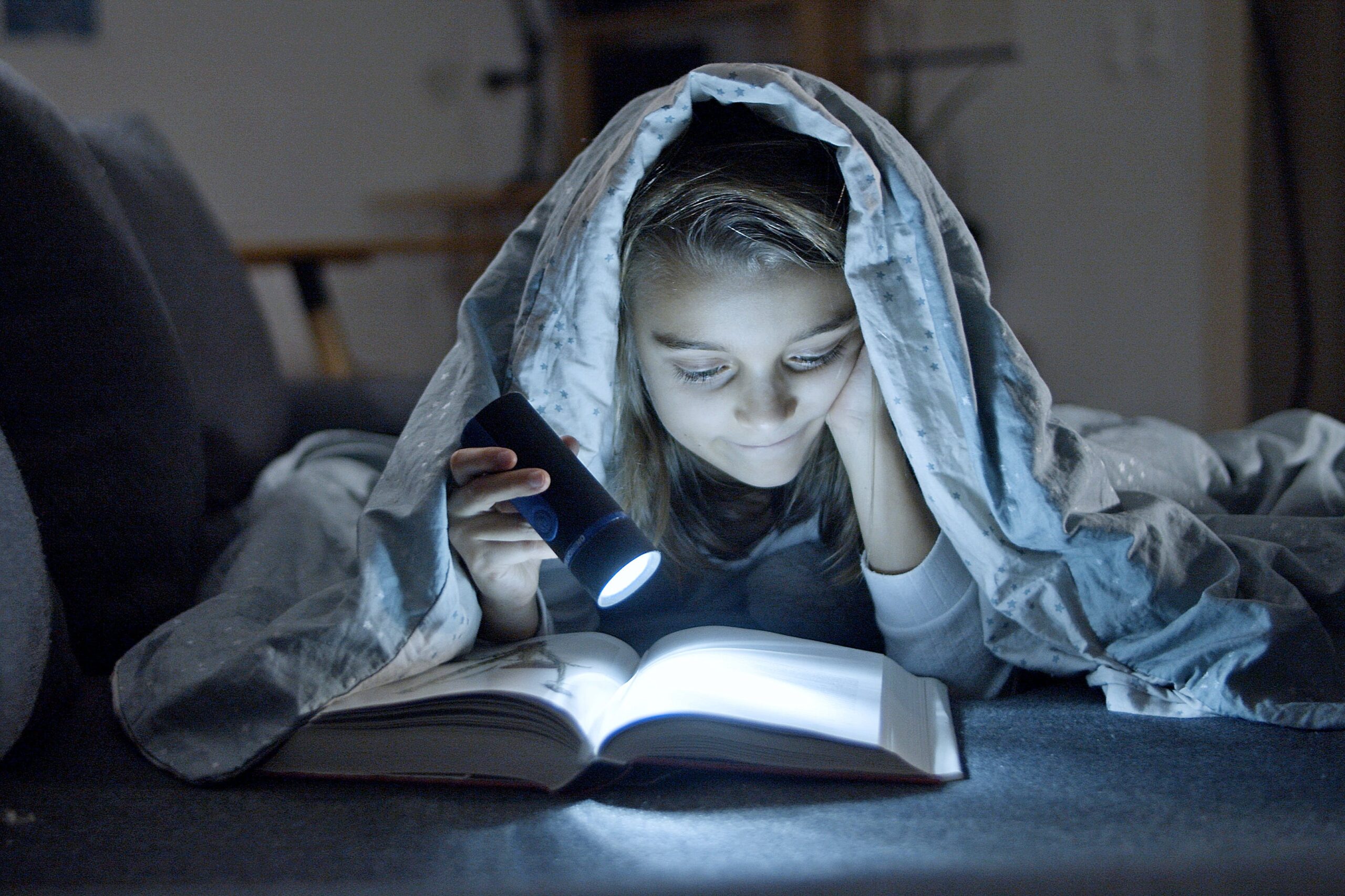 Una persona leyendo un libro bajo una manta con una linterna sobre cuentos para mimir.